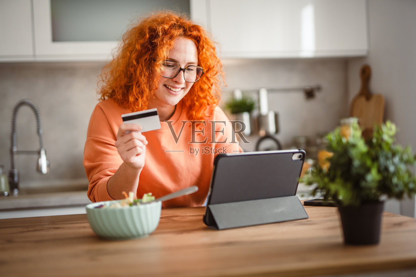 女人吃沙拉，使用平板电脑和信用卡付款。照片摄影图片