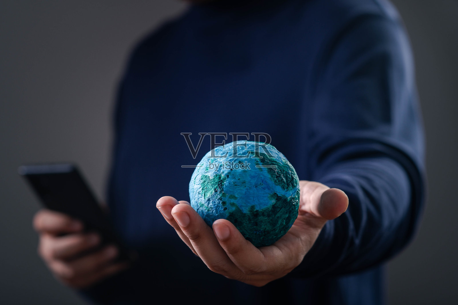 一个人手持一个小地球仪，同时使用智能手机，象征着科技与全球意识。照片摄影图片