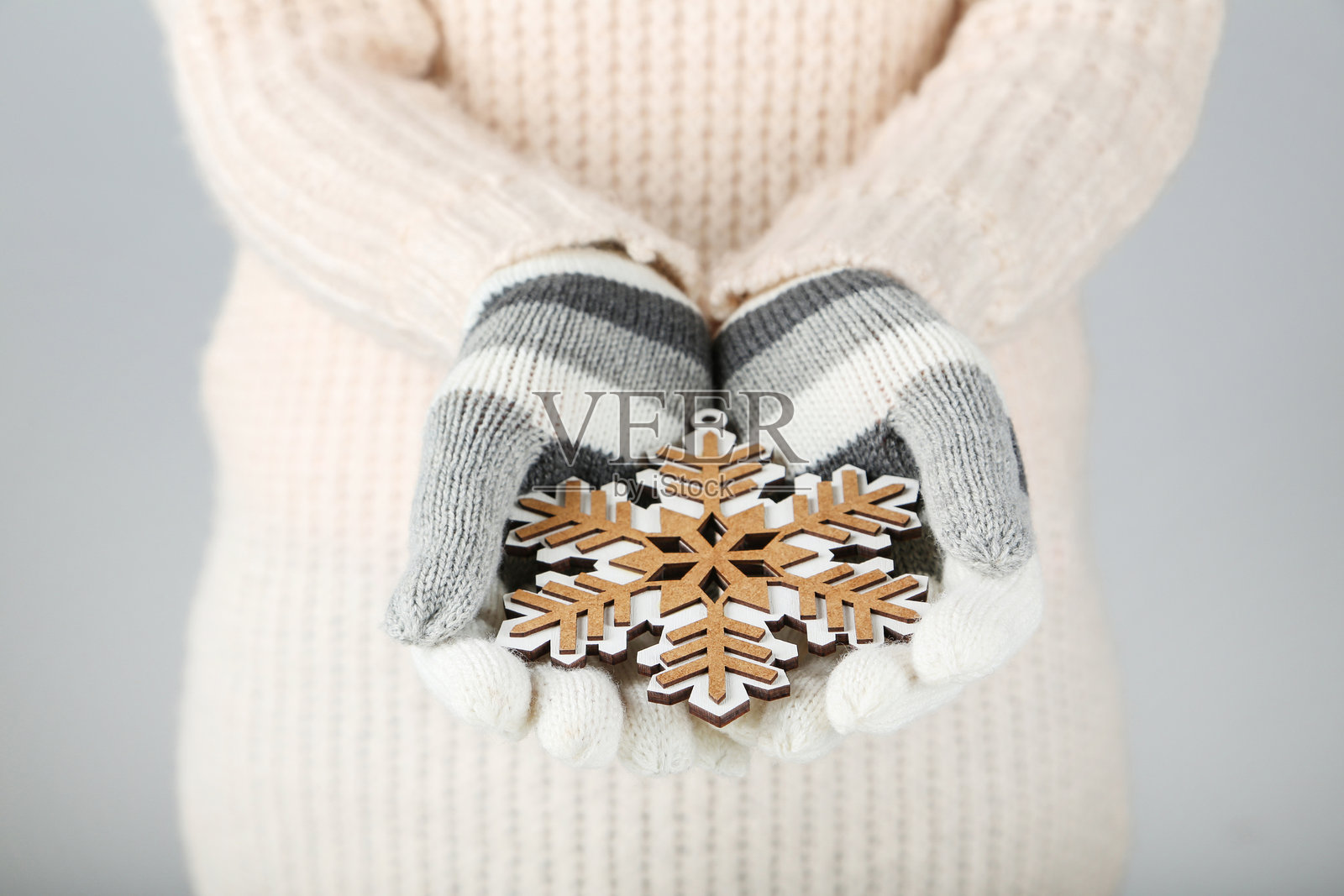 戴着针织手套的手握着木制雪花，背景为灰色照片摄影图片