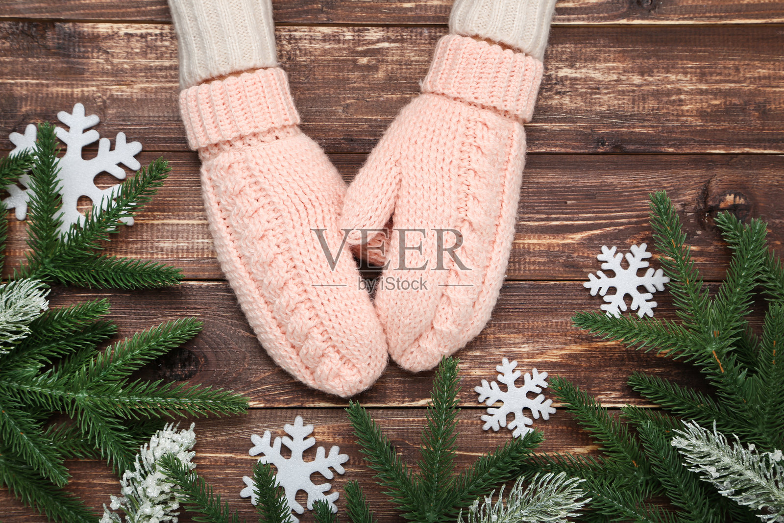 手戴着编织手套，桌上有雪花和松树枝照片摄影图片