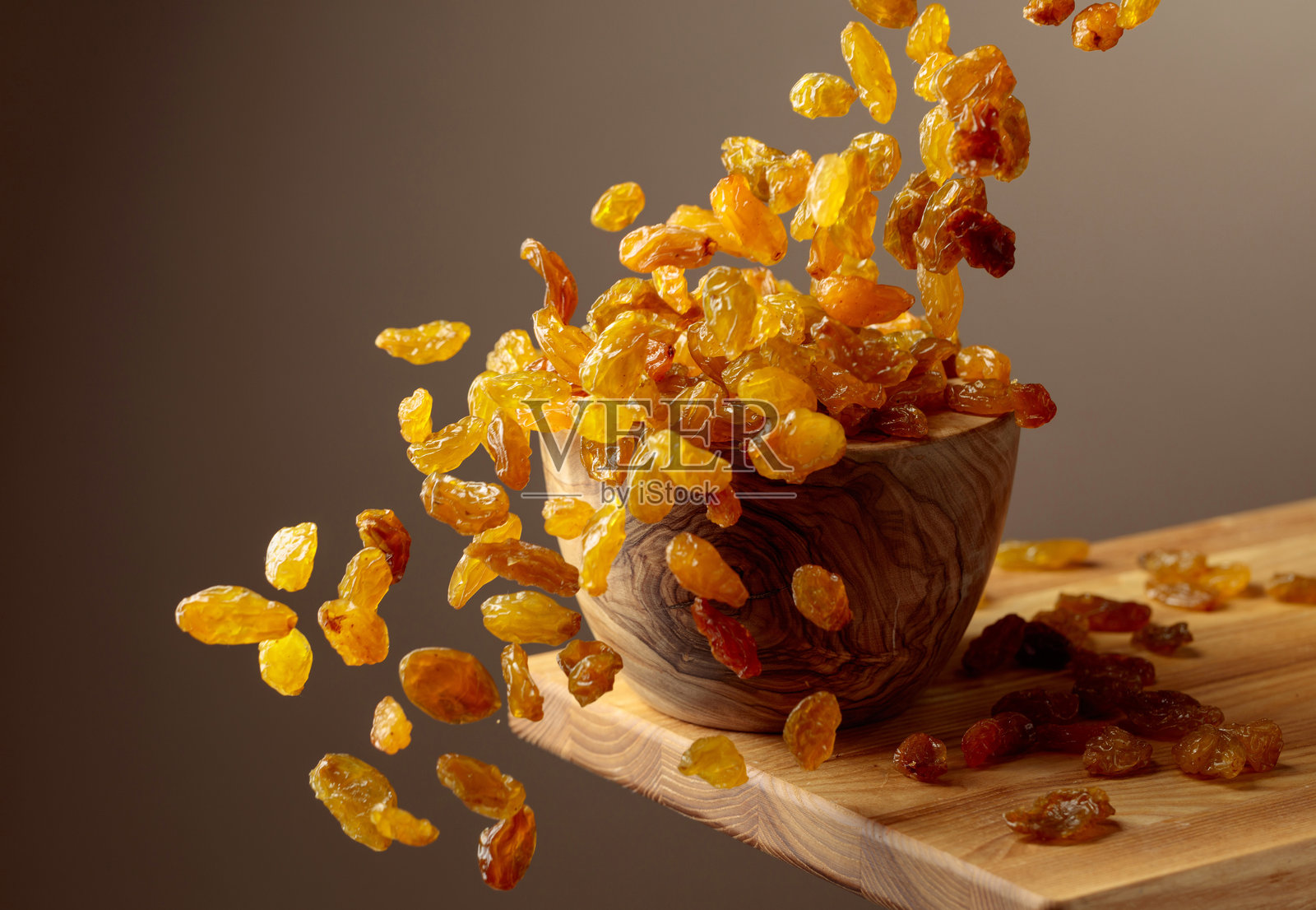 黄色的苏丹娜葡萄干倒入一个木碗中。照片摄影图片