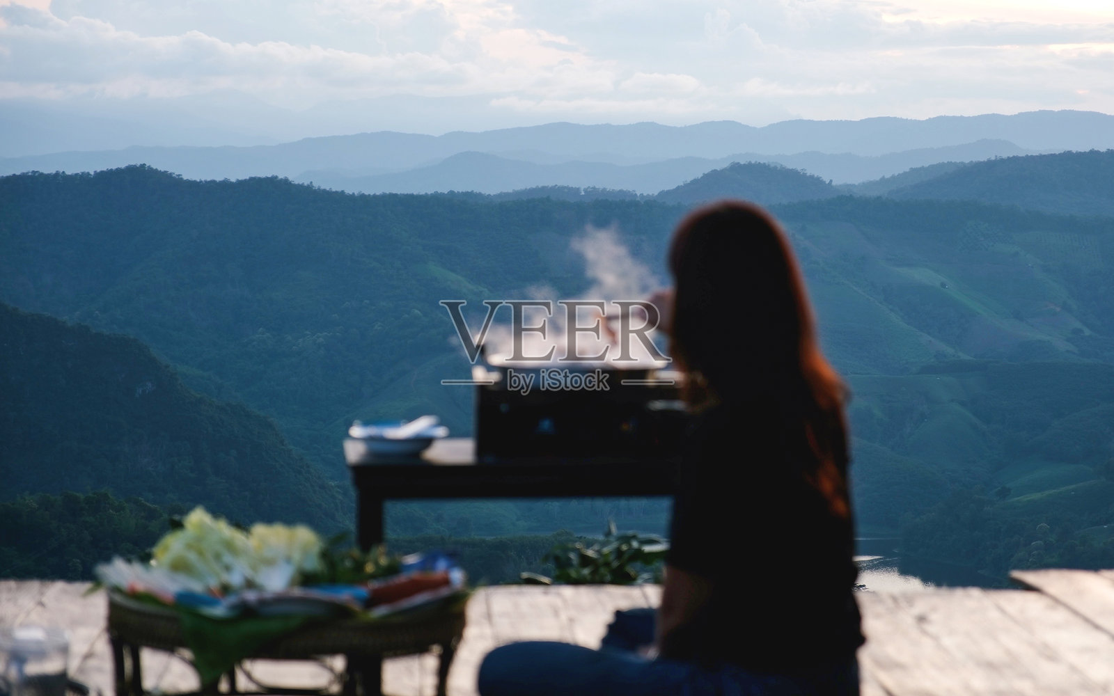 模糊的女人在烹饪和享用Moo Kata，泰式烧烤猪肉，背景是美丽的山景照片摄影图片