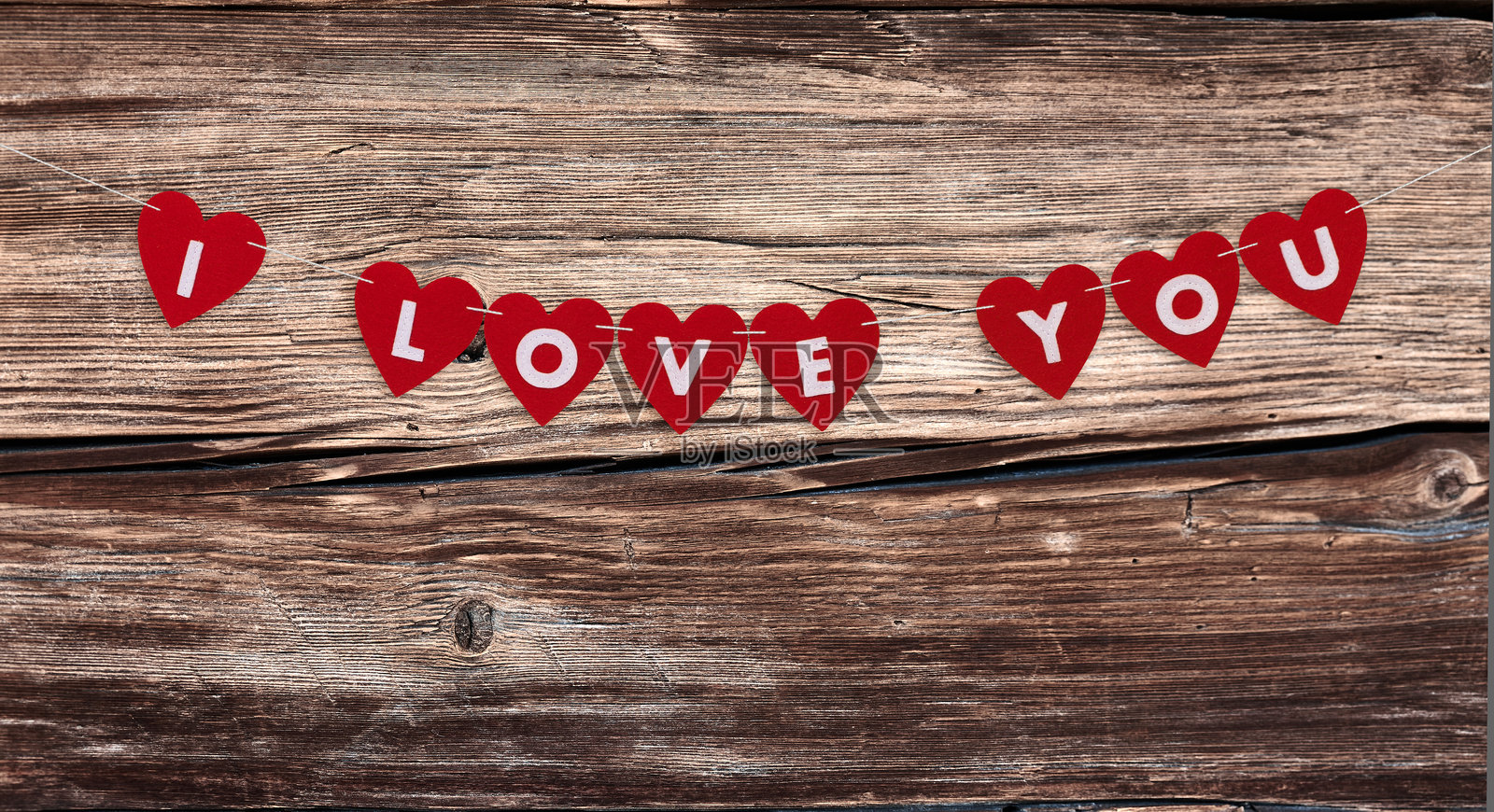 红色心形花环，上面挂着“我爱你”字样，背景是粗糙的木板。照片摄影图片