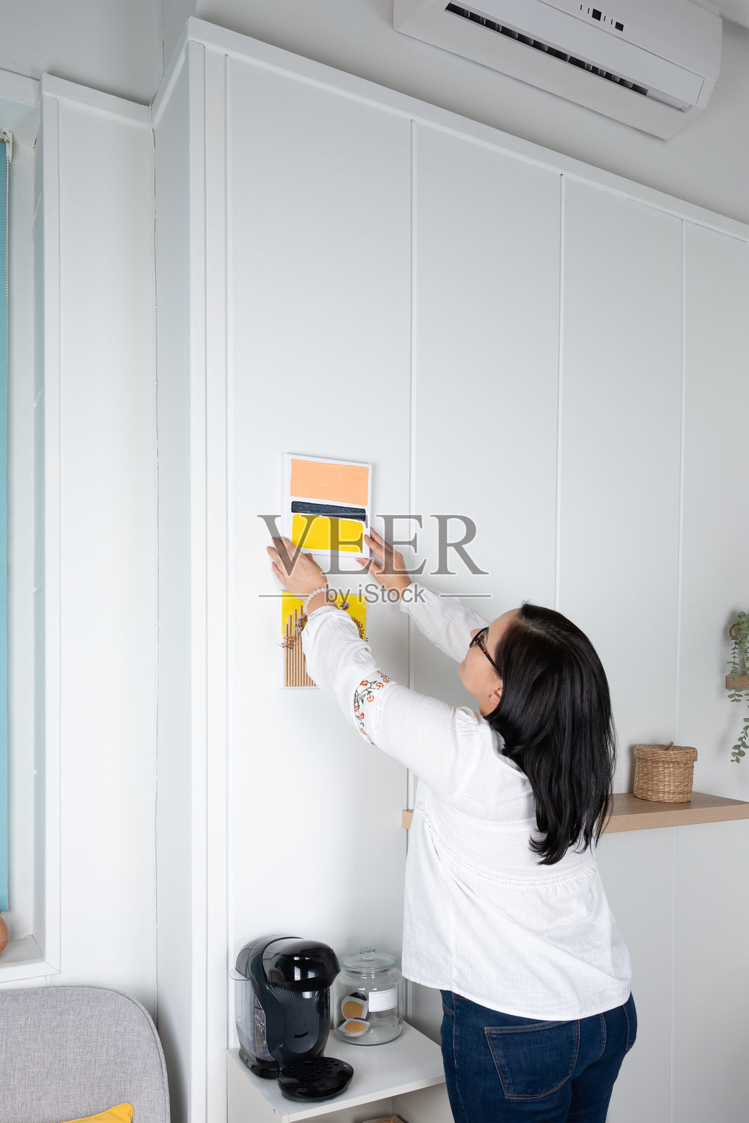 成熟的女性在明亮的房间里挂着自己制作的两幅画。照片摄影图片