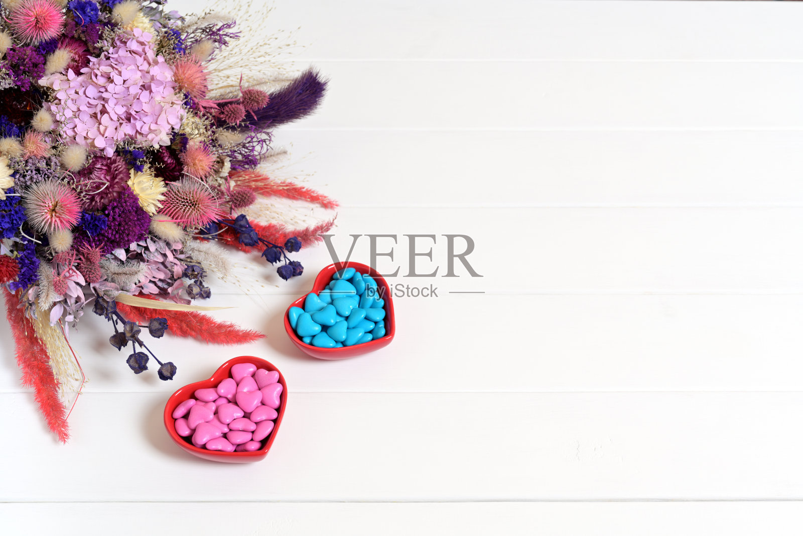 白色木质背景上的干花束与红色碗中的心形糖果照片摄影图片