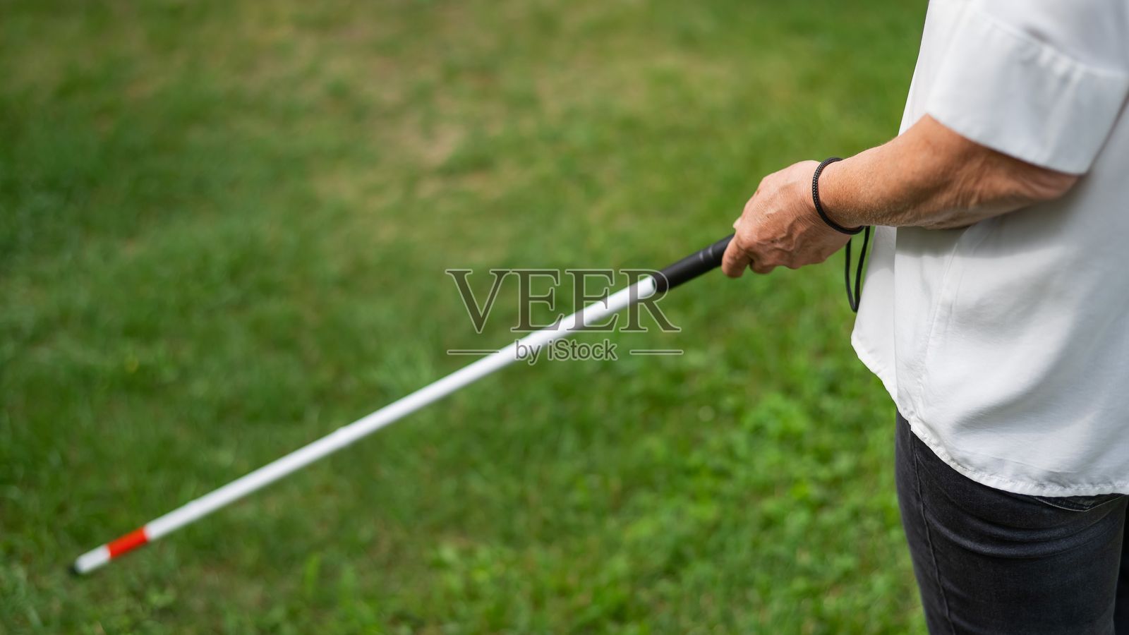一位老年女性在公园散步时，使用触觉手杖的腿部特写。照片摄影图片