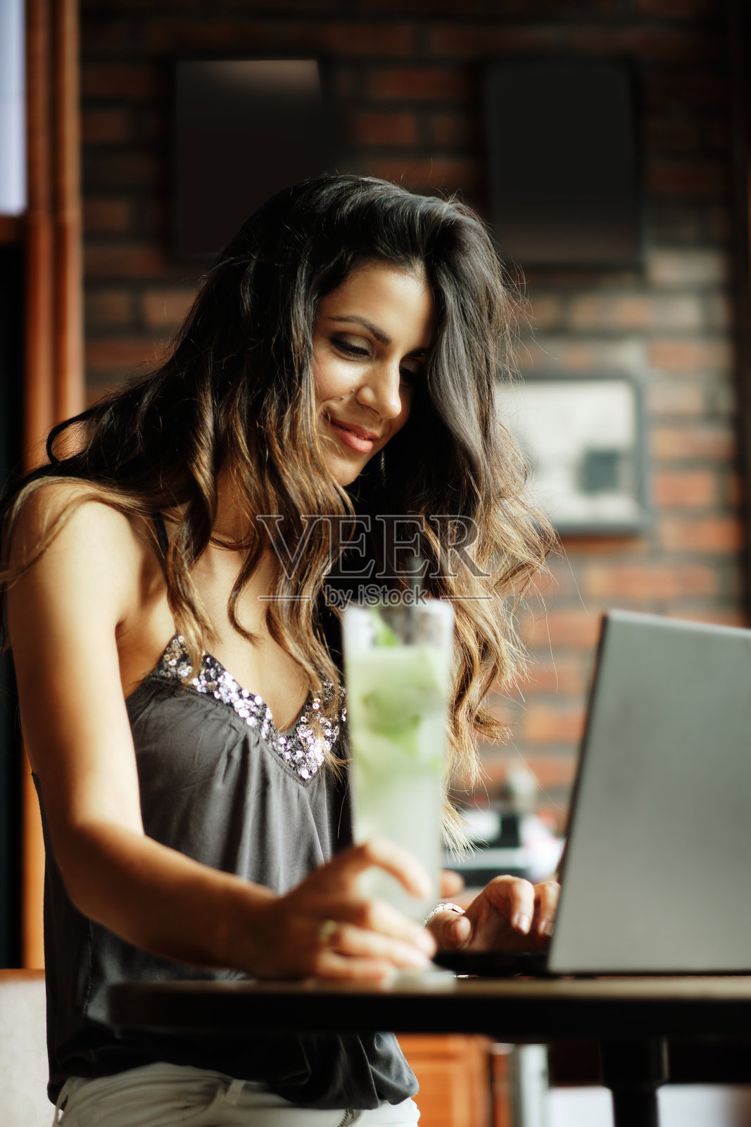 一位美丽的年轻女性，长发黑色，正坐在酒吧里使用笔记本电脑。照片摄影图片