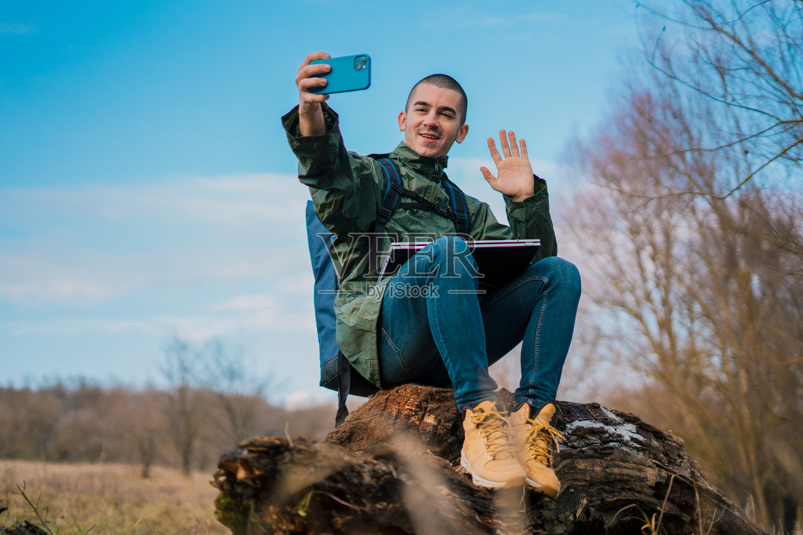 一位年轻帅气的男士在大自然中放松，背着一个大背包，微笑着自拍——自然与现代科技的完美结合。照片摄影图片
