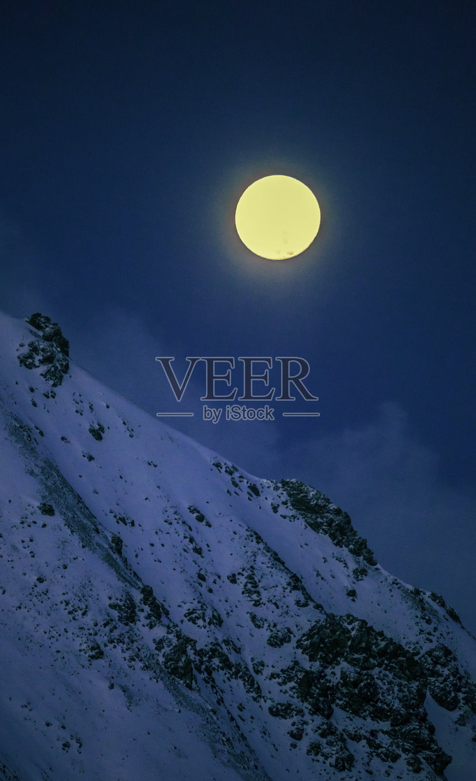 明亮的圆形满月高悬在岩石山坡上，构成了一个天际景观。照片摄影图片