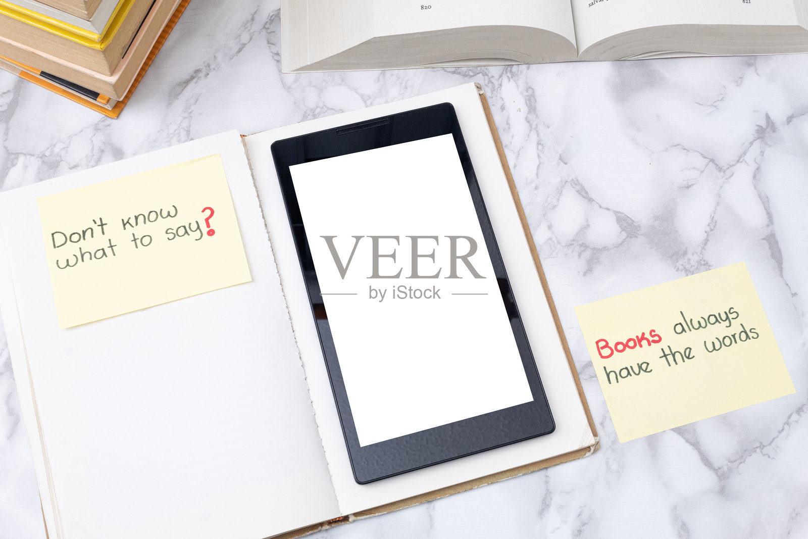 电子阅读器放在一本打开的书上，书中夹着关于阅读的励志便签。优雅的大理石桌子上，数字阅读器的空白屏幕旁边放着几本书。不知道该说什么？书籍总是有话要说。照片摄影图片