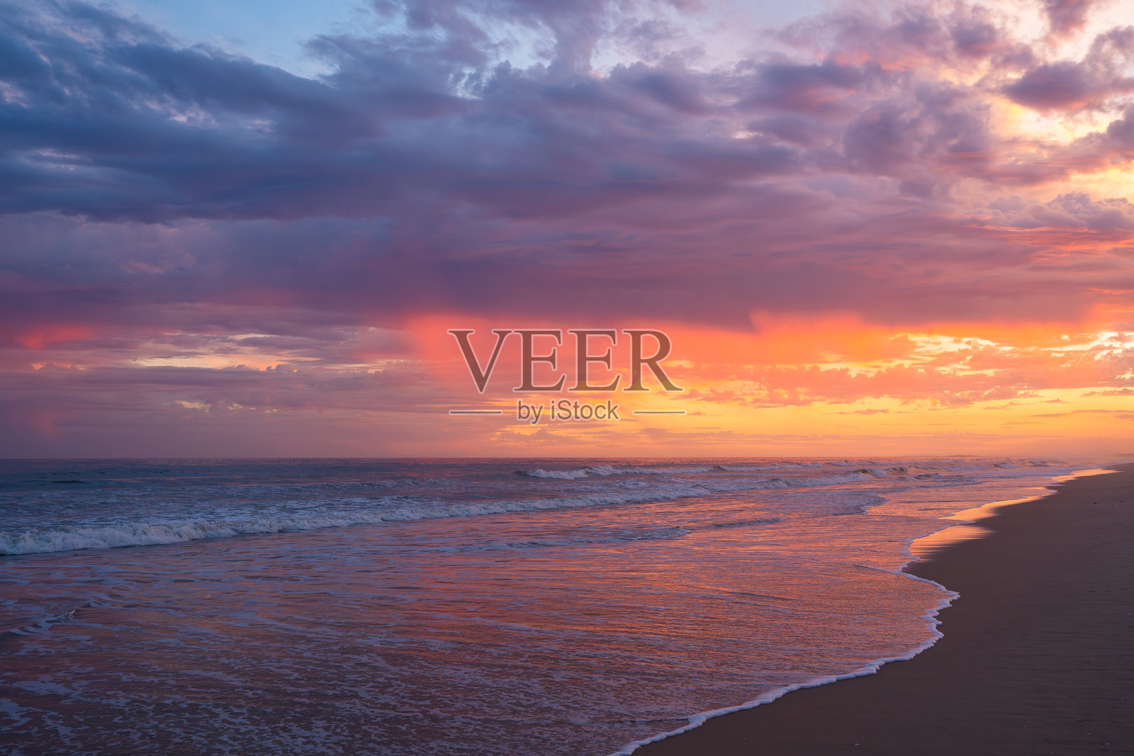 波浪在色彩斑斓、戏剧性的天空下涌动，天空被深邃的日落色调渲染。照片摄影图片