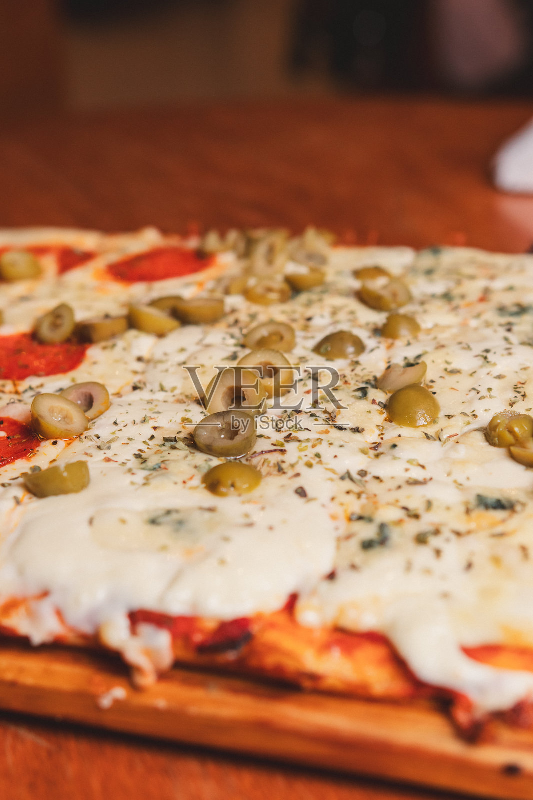 特写镜头展示了一块满是奶酪、意大利香肠和橄榄的比萨饼，放在木桌上。照片摄影图片