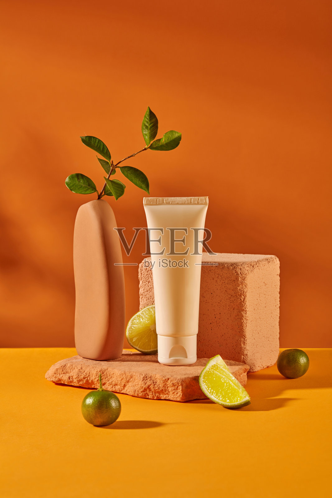 一个没有标签的化妆管的正面视图被放置在一个石头平台上，周围是柠檬和金橘。明亮的背景与黄色和橙色的颜色。化妆品模型。照片摄影图片