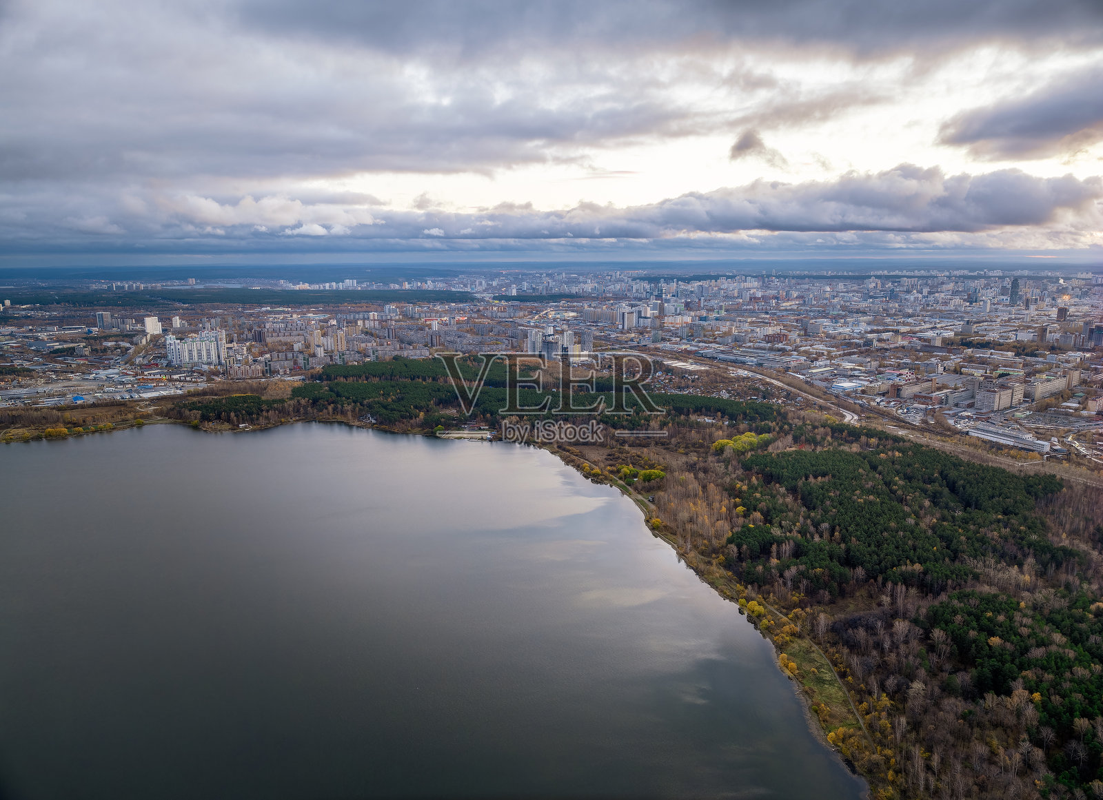 日落时湖岸的秋林，地平线上的城市，鸟瞰照片摄影图片