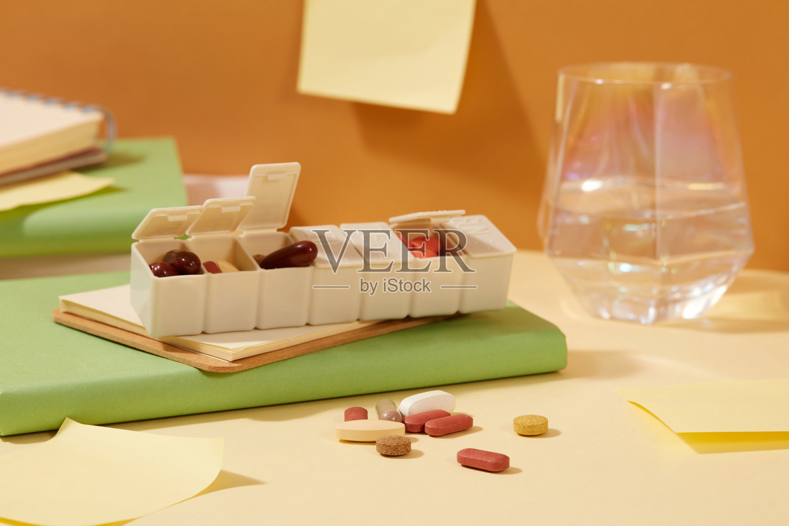 一个装有不同大小和颜色的药片的日常药盒。桌上放着一杯水和笔记本。医学主题的复制空间。照片摄影图片