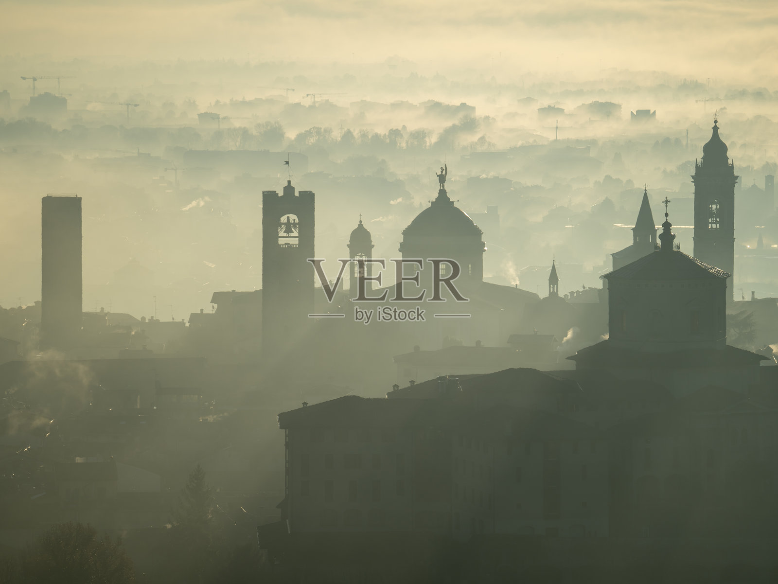 意大利贝加莫。令人惊叹的空中景观，雾气从平原升起，在日出时覆盖了老城区。温暖的颜色。贝加莫是意大利最美丽的城市之一照片摄影图片