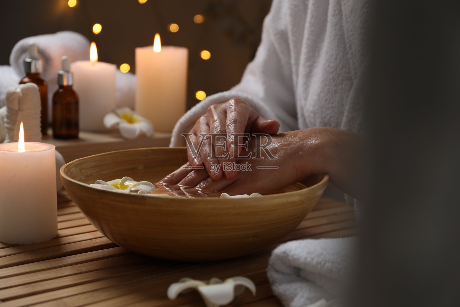 一个女人把手浸在一碗水里，木桌上放着鲜花，特写。矿泉疗法照片摄影图片