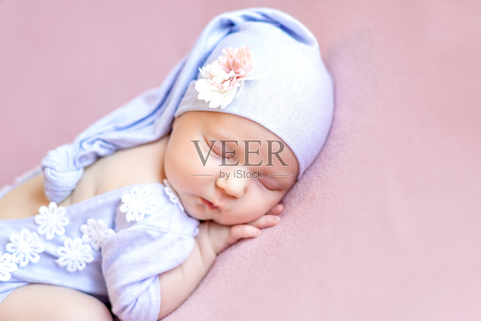 穿着蓝色连体衣的小女孩在粉色背景上，头戴帽子，甜美地趴着睡觉，特写肖像。照片摄影图片