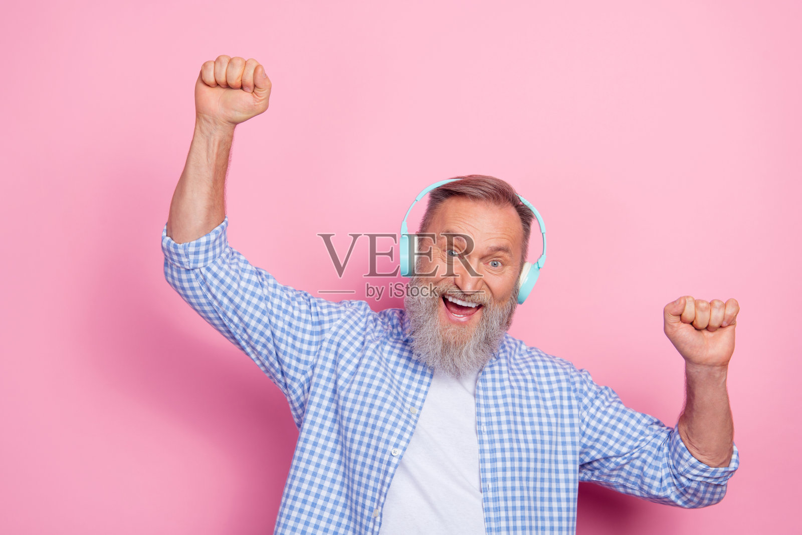 兴奋快乐的老年人举起拳头跳舞，享受新播放列表，背景为粉色。照片摄影图片