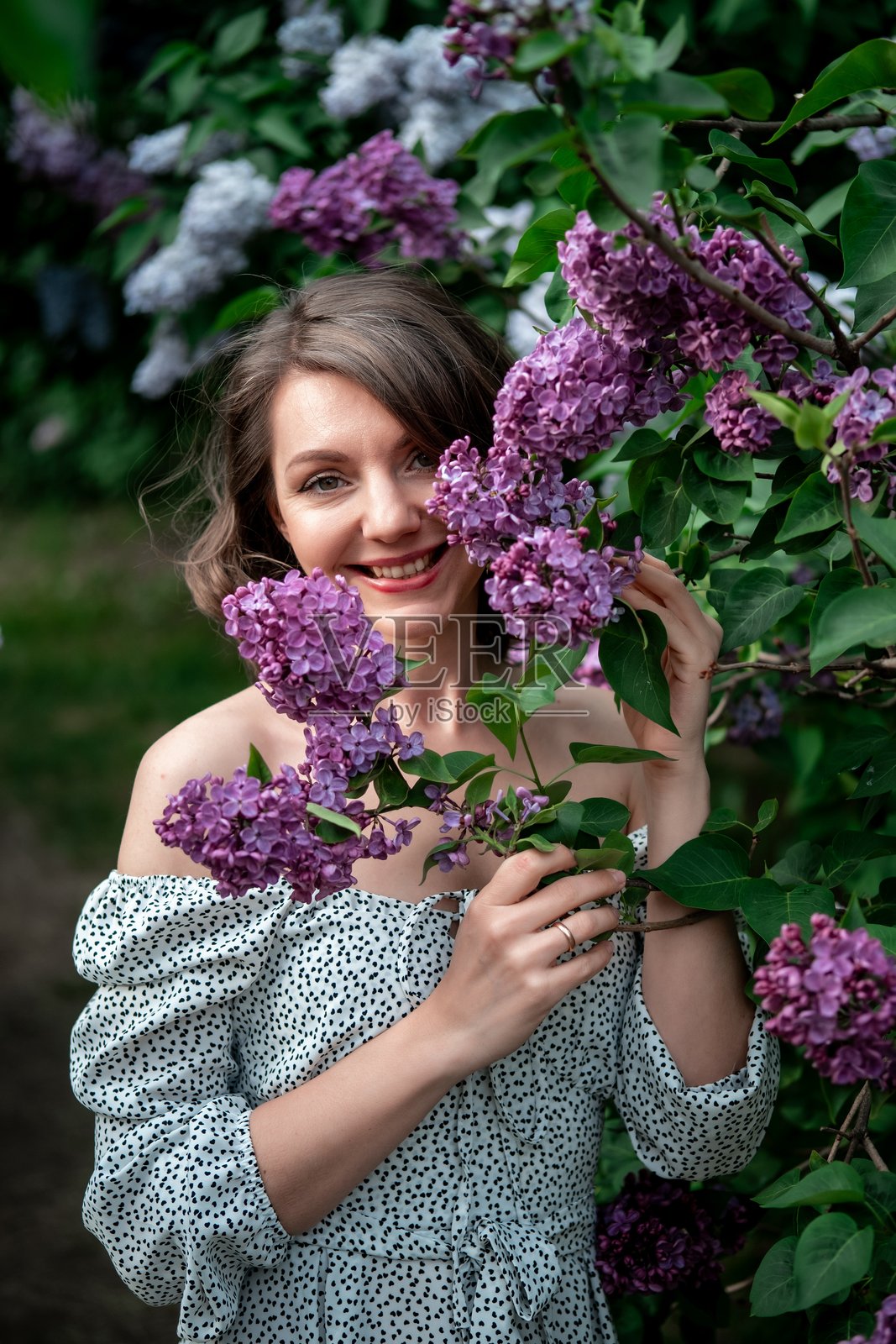 一个女孩在蓝莓花丛中，一个美丽的年轻女孩在紫丁香灌木丛旁的公园里，一个女孩在夏天的公园里享受大自然和花香。照片摄影图片