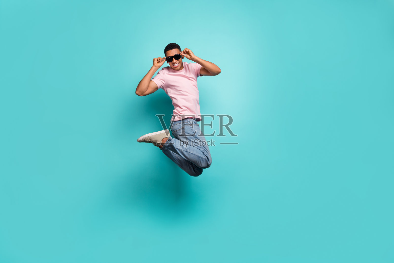全身照，帅气的男孩穿着粉色T恤在空旷的空间中高高跳起，背景为青色。照片摄影图片