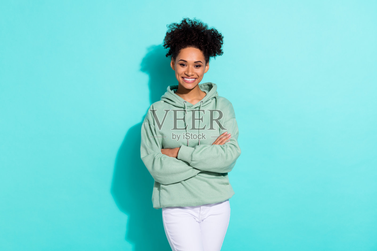 微笑灿烂、双臂交叉的美丽积极人物肖像，背景为明亮的青绿色。照片摄影图片