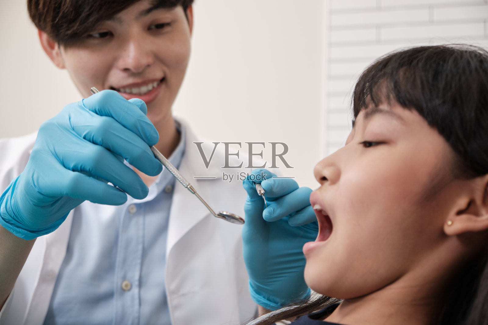 亚洲男性牙医在牙科诊所检查和检查女孩的牙齿。照片摄影图片