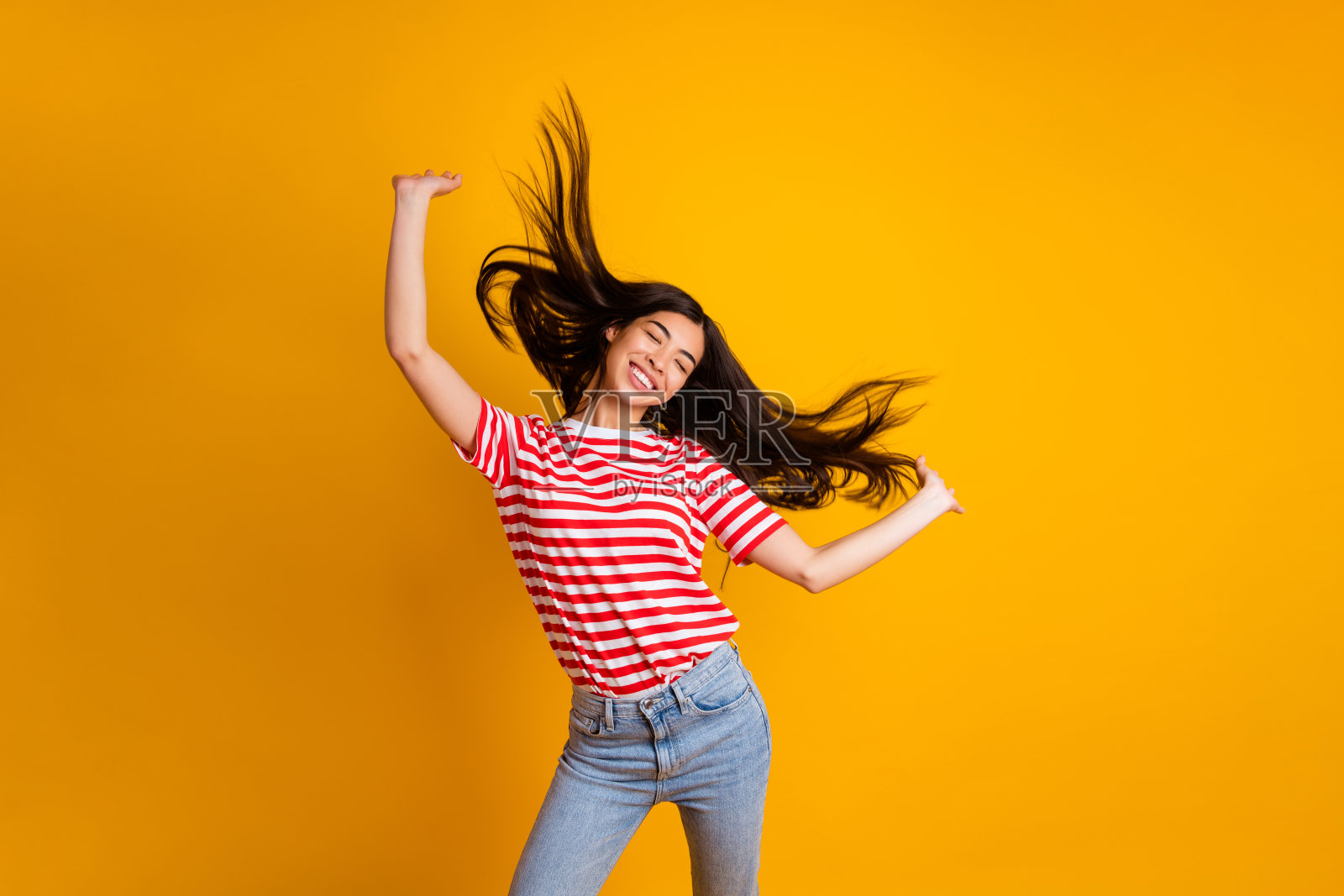 快乐迷人的黑发女孩穿着白色和红色T恤，悠闲地跳舞，背景为黄色。照片摄影图片