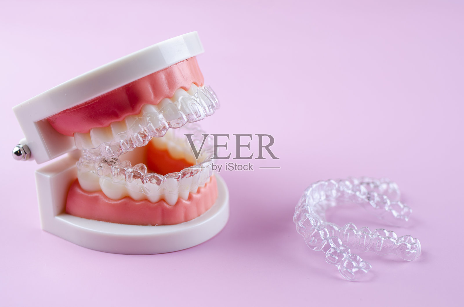特写。粉色背景上的透明矫正器用于人工牙齿照片摄影图片
