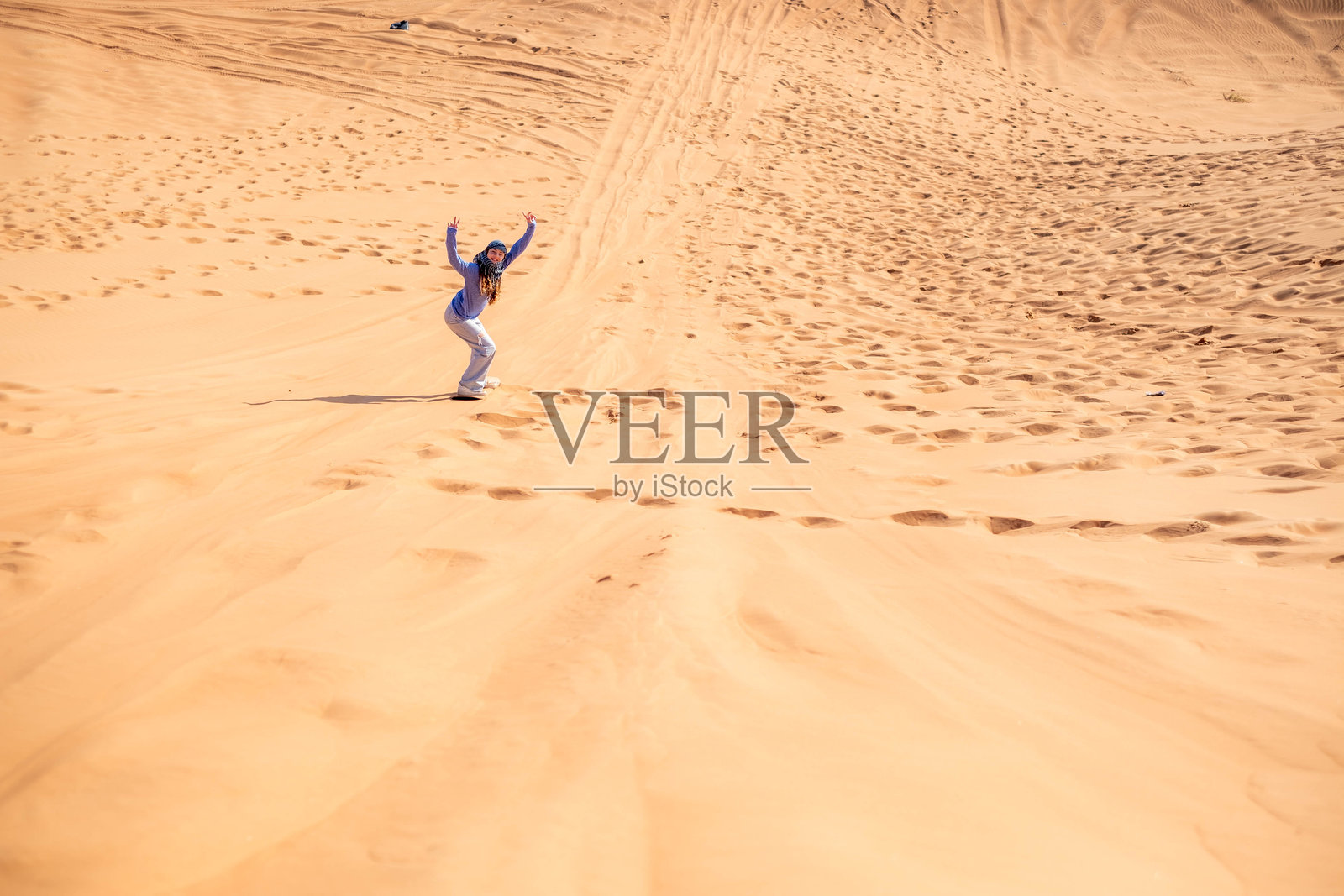 快乐的少女在沙漠中滑沙，举起双手，满脸幸福。照片摄影图片