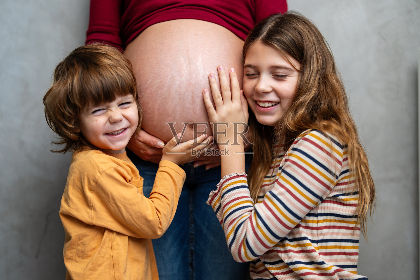 可爱的兄妹们开心地期待着新家庭成员的到来。他们在抚摸母亲的肚子。照片摄影图片