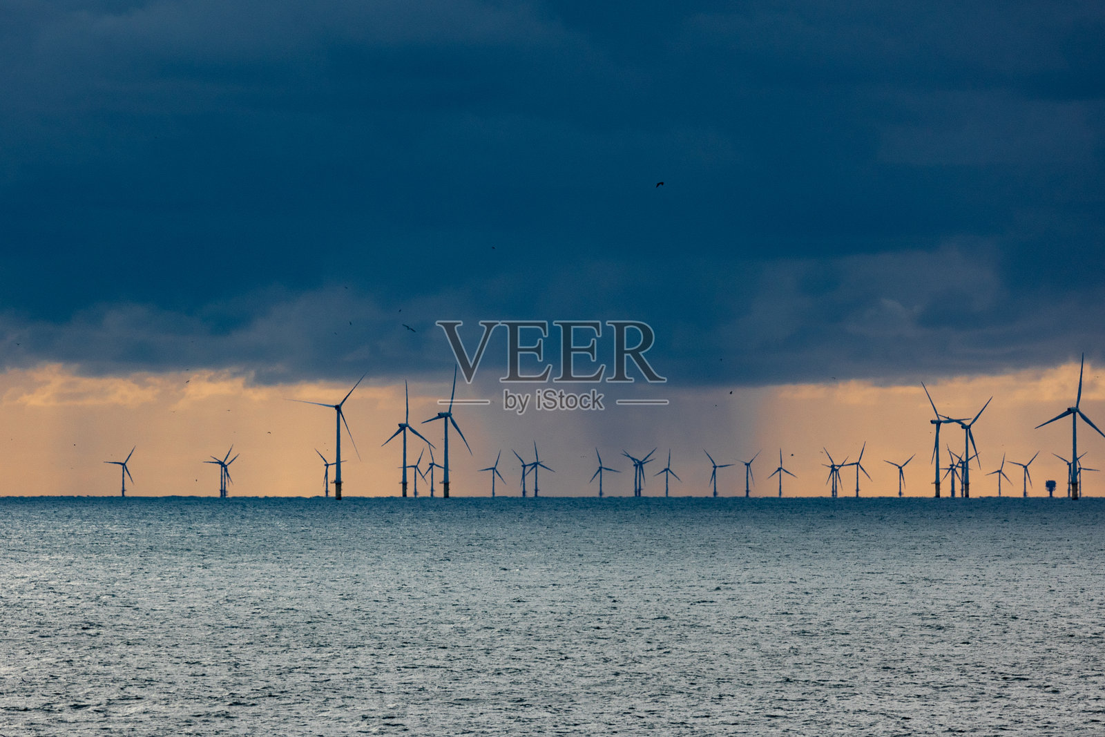 乌云密布的雷暴，雨水倾泻在北海上，背景中有风力涡轮机的剪影。照片摄影图片