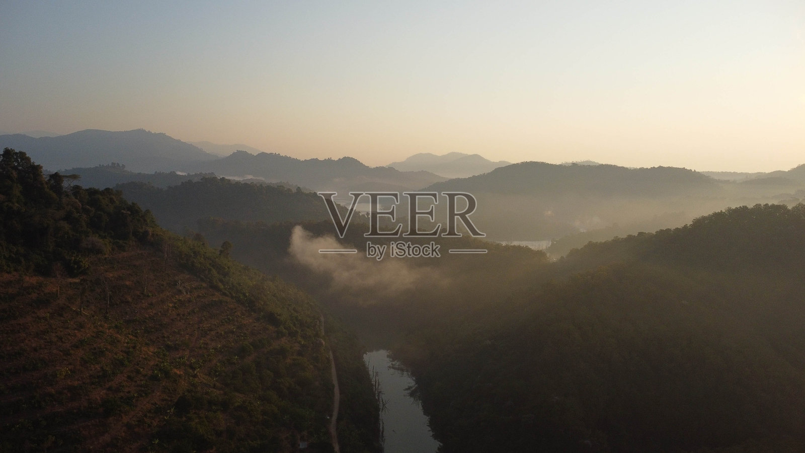 冬季山上的美丽日出。阳光洒在宁静的山景上，覆盖着热带树木和清澈的河流，清晨的氛围宁静而祥和。照片摄影图片