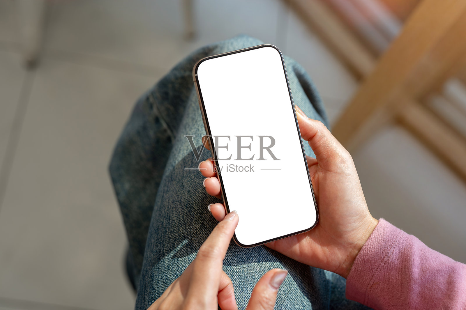 一位穿着牛仔裤的女性坐在室内，俯视近距离使用智能手机。照片摄影图片