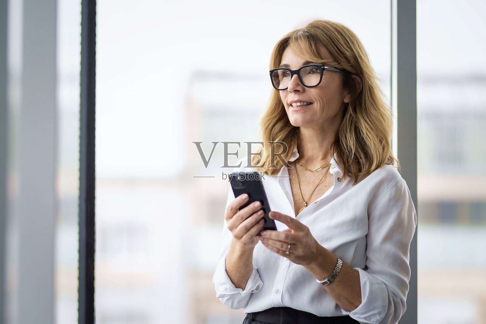 金发女性在办公室里拿着智能手机。照片摄影图片