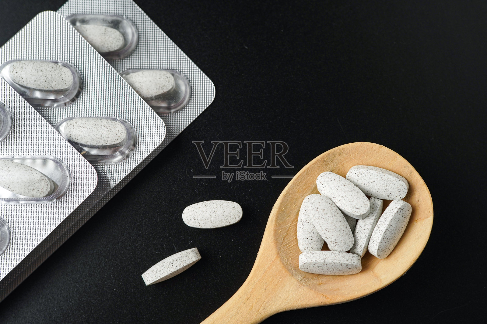 黑色背景上的木勺中装有白色药丸、药片和胶囊的泡罩包装照片摄影图片