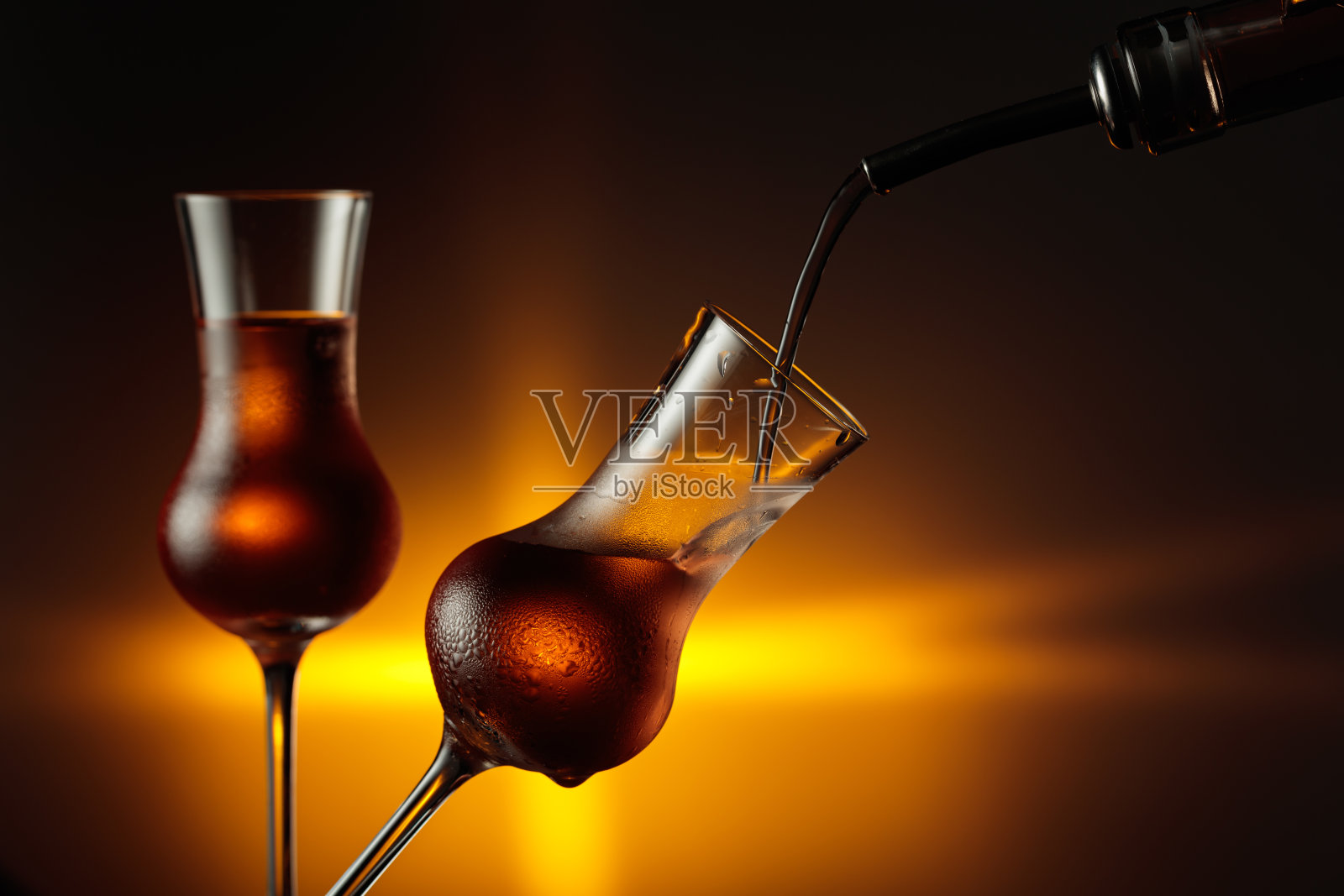 将酒精饮料倒入带有天然冰块的蒸汽玻璃杯中。照片摄影图片