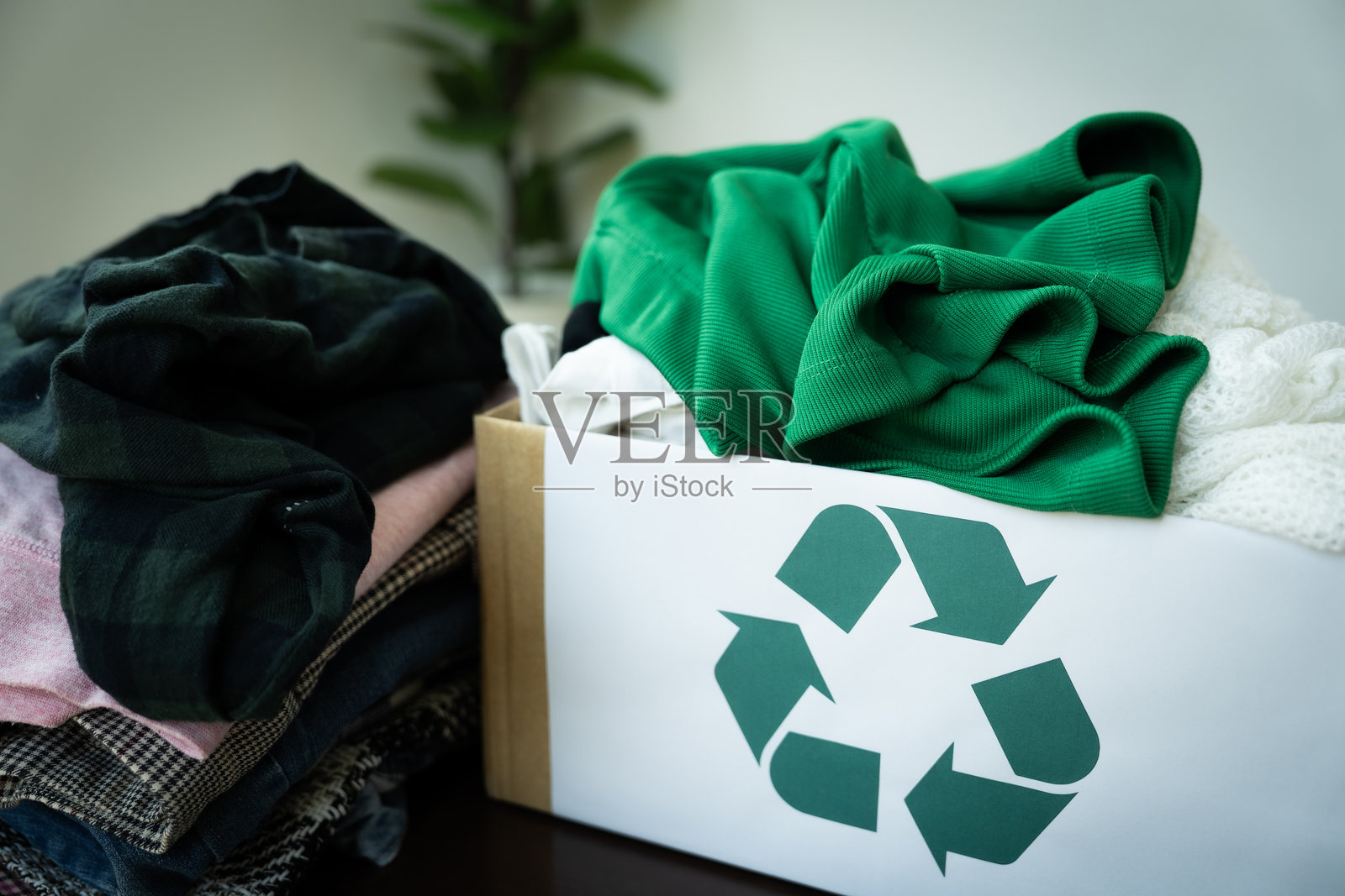 一箱衣物堆在一个带有绿色回收标志的箱子上。衣物颜色和风格各异，箱子里装得满满的。传达了回收和再利用衣物的概念。照片摄影图片