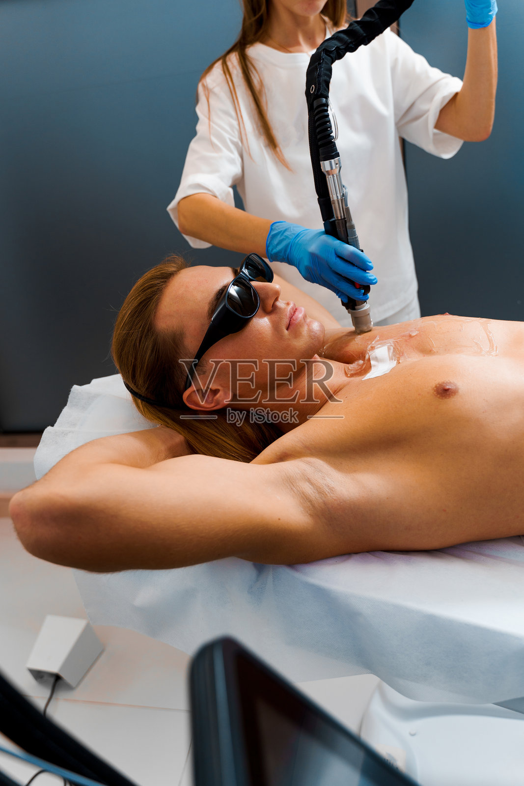 通过超声波激光脱毛去除多余的体毛。男性激光脱毛。男性在接受脱毛师的胸部激光脱毛。照片摄影图片