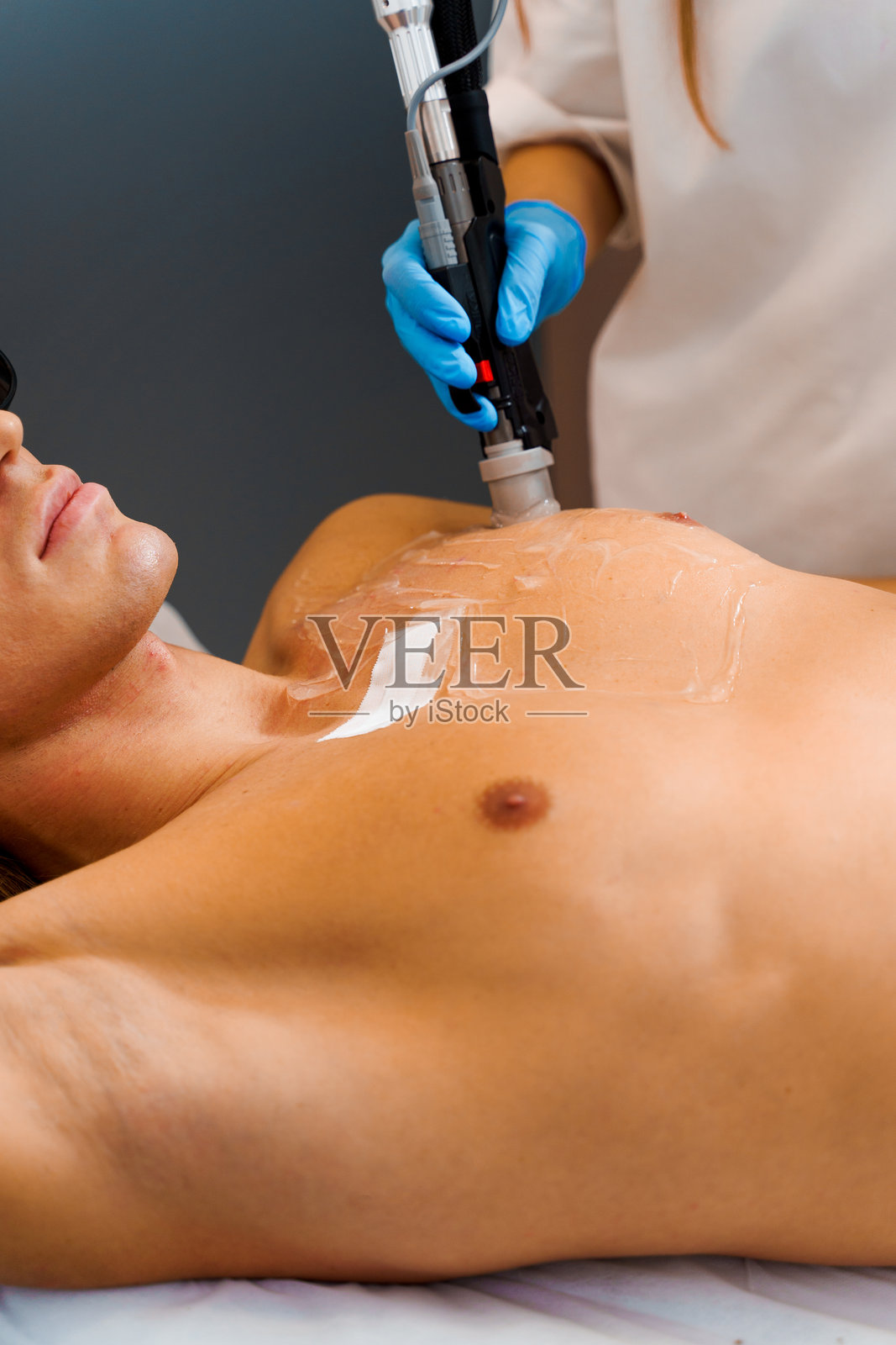 通过超声波激光脱毛去除多余的体毛。男性激光脱毛。男子在脱毛师的操作下进行胸部激光脱毛。照片摄影图片