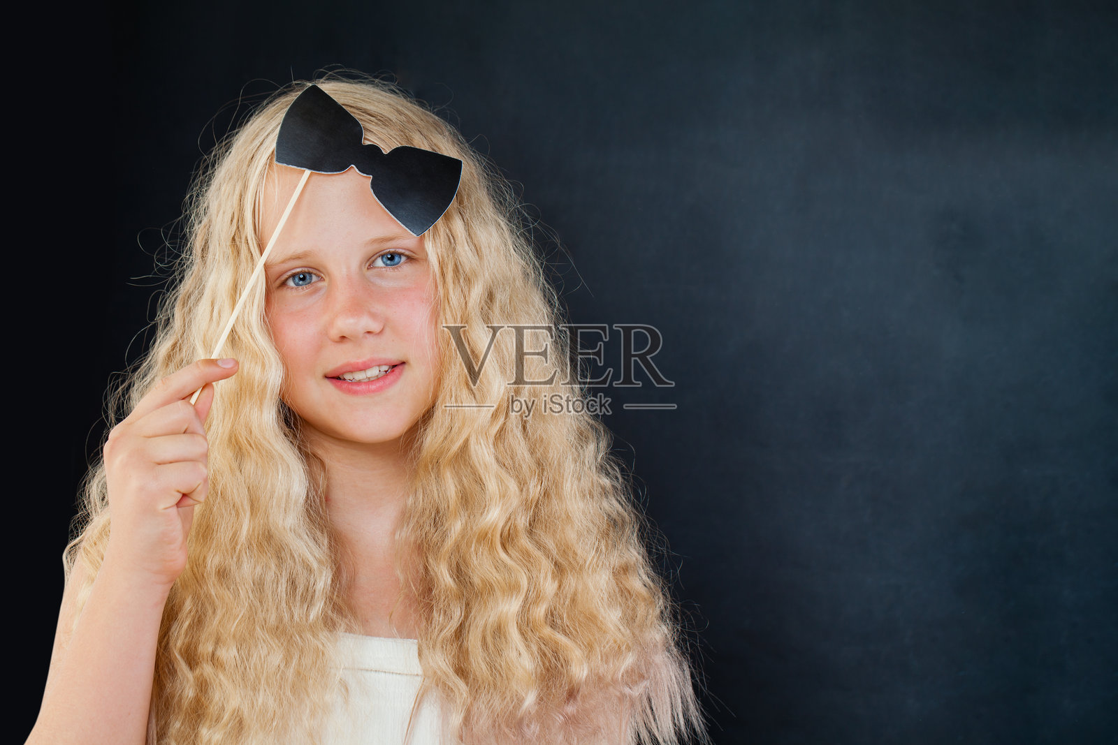 微笑的年轻女孩在黑色背景下摆姿势，手持照片亭道具和蝴蝶结照片摄影图片