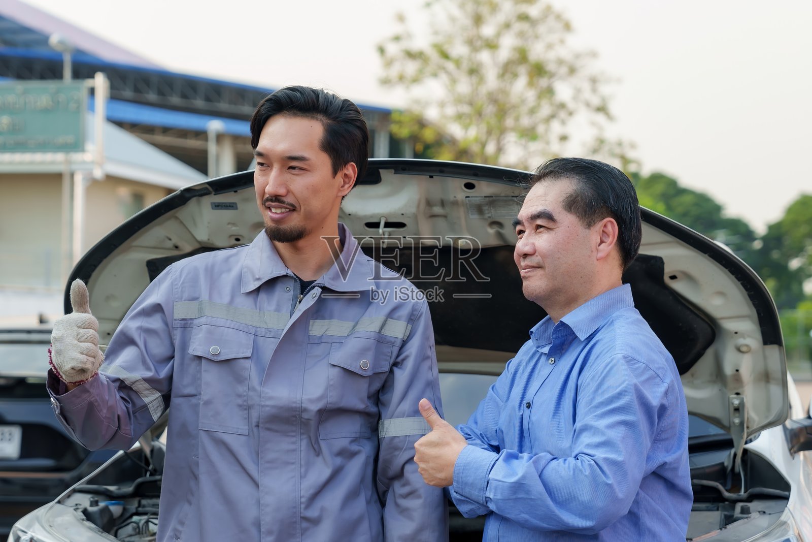 机械师和顾客竖起大拇指，展示成功的汽车修理和卓越的客户满意度。突显汽车服务中的信任和良好关系。照片摄影图片