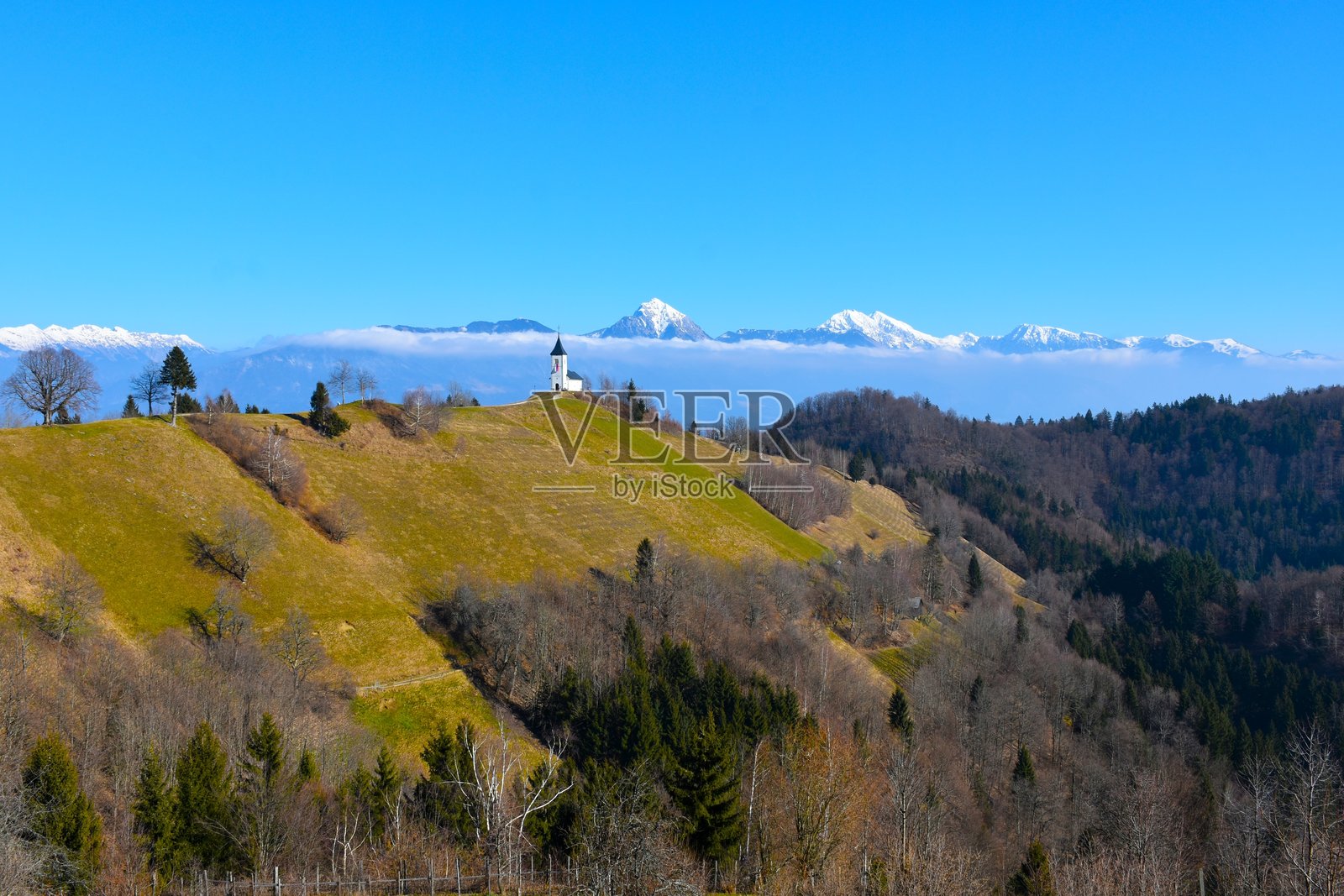 斯洛文尼亚戈伦斯基地区，贾姆尼克的圣普里穆斯和费利西亚教堂下方的草坡，以及背景中的雪覆盖山峰。照片摄影图片