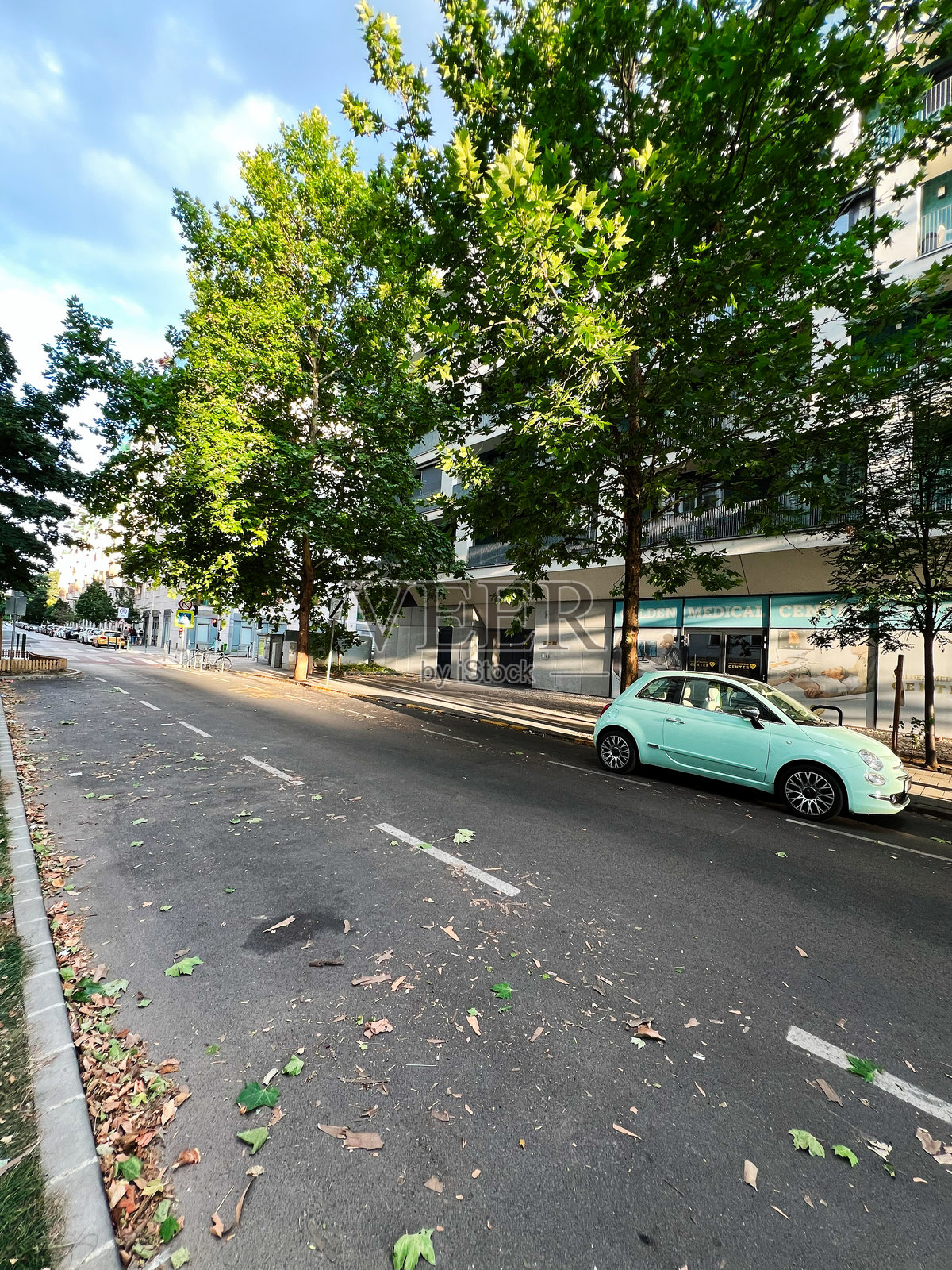 阳光明媚的天空下，城市街道上停着一辆小型绿色汽车照片摄影图片