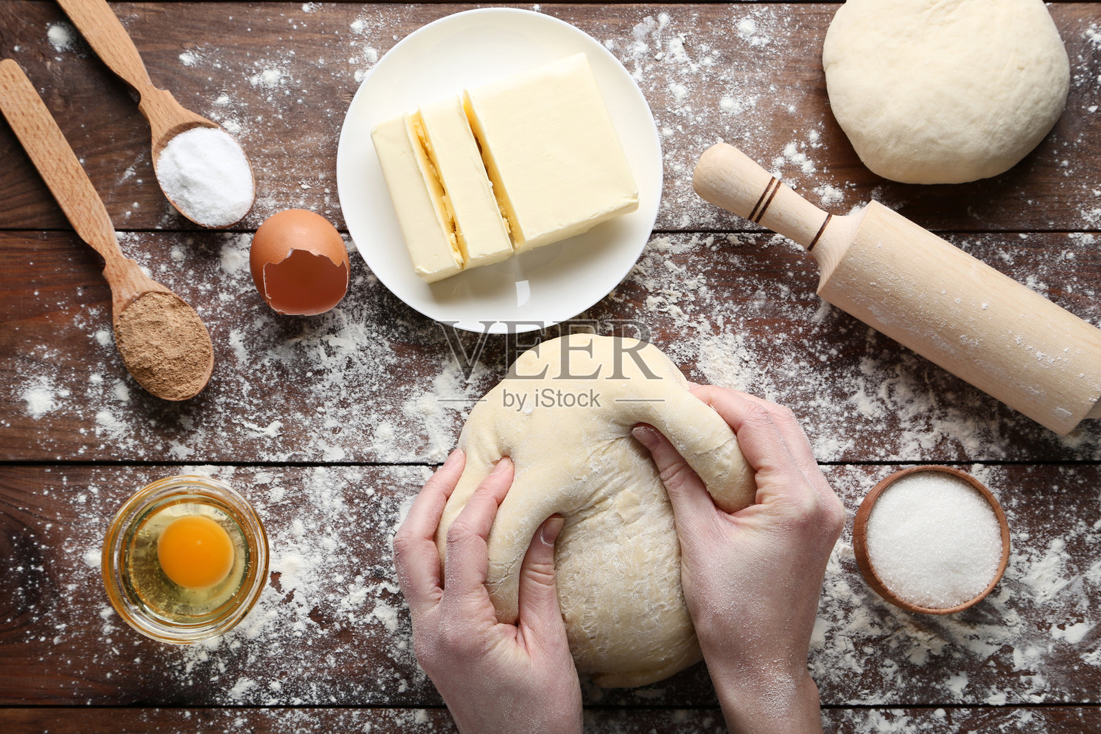 女性的手在木桌上用盘子揉面团和黄油，旁边有鸡蛋。照片摄影图片