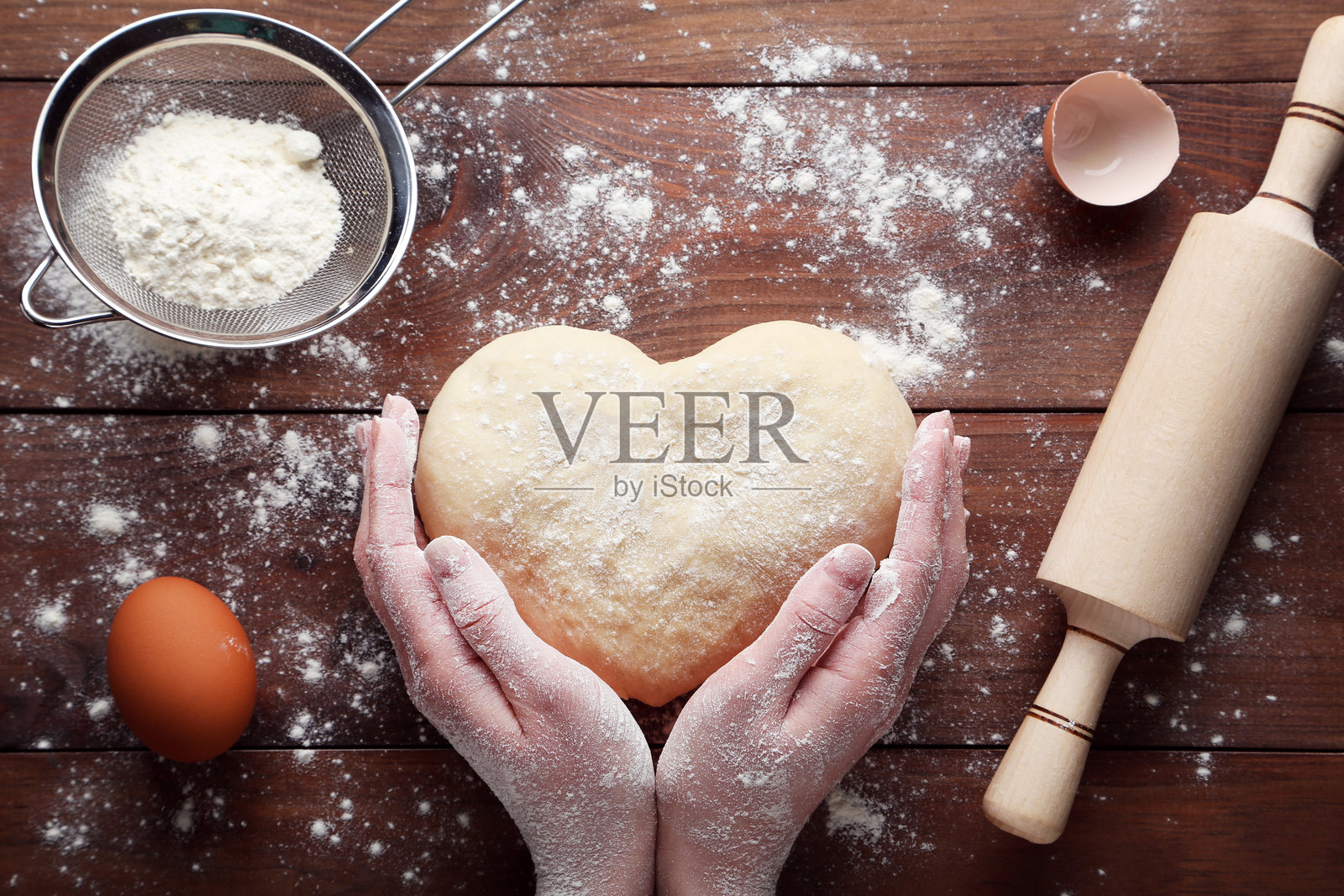 女性手握着心形生面团，放在木桌上照片摄影图片