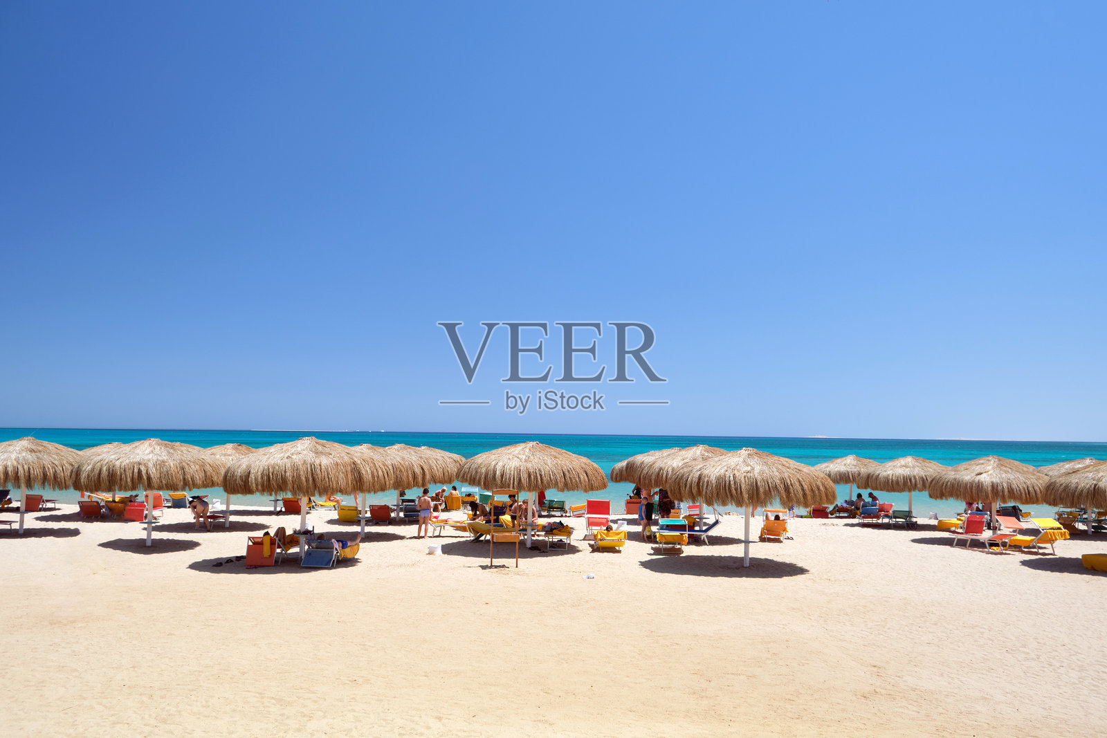 热带海滩上的草遮阳伞，旁边是休息的躺椅，背景是夏季湛蓝的天空。照片摄影图片