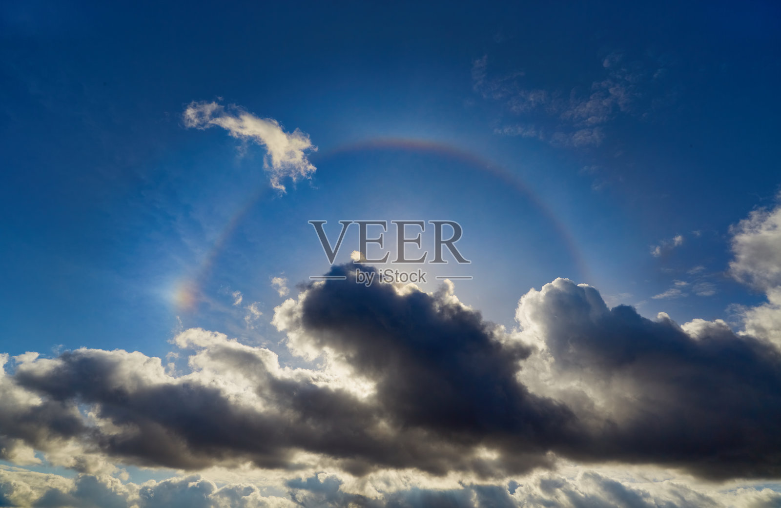 蓝天白云下的光环现象。自然光学现象，表现为在高空云层中太阳周围的发光环。照片摄影图片