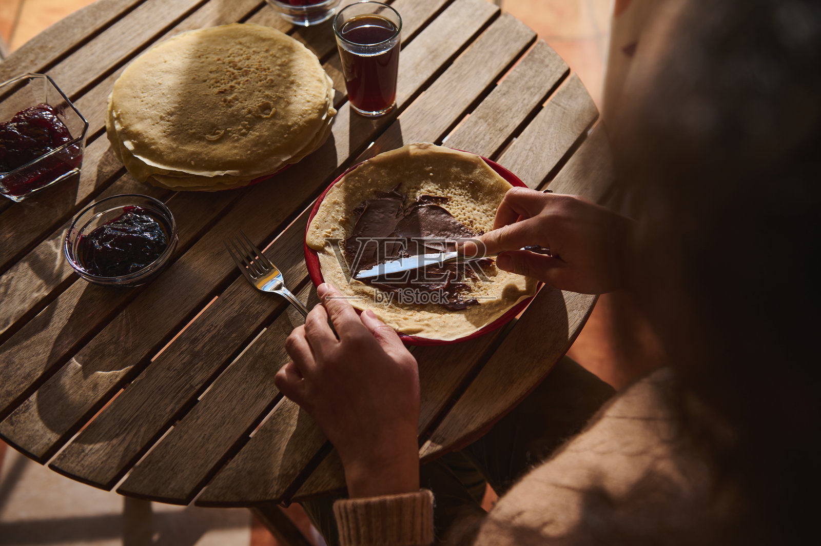 在木桌上涂抹巧克力酱的人员，旁边有果酱。照片摄影图片