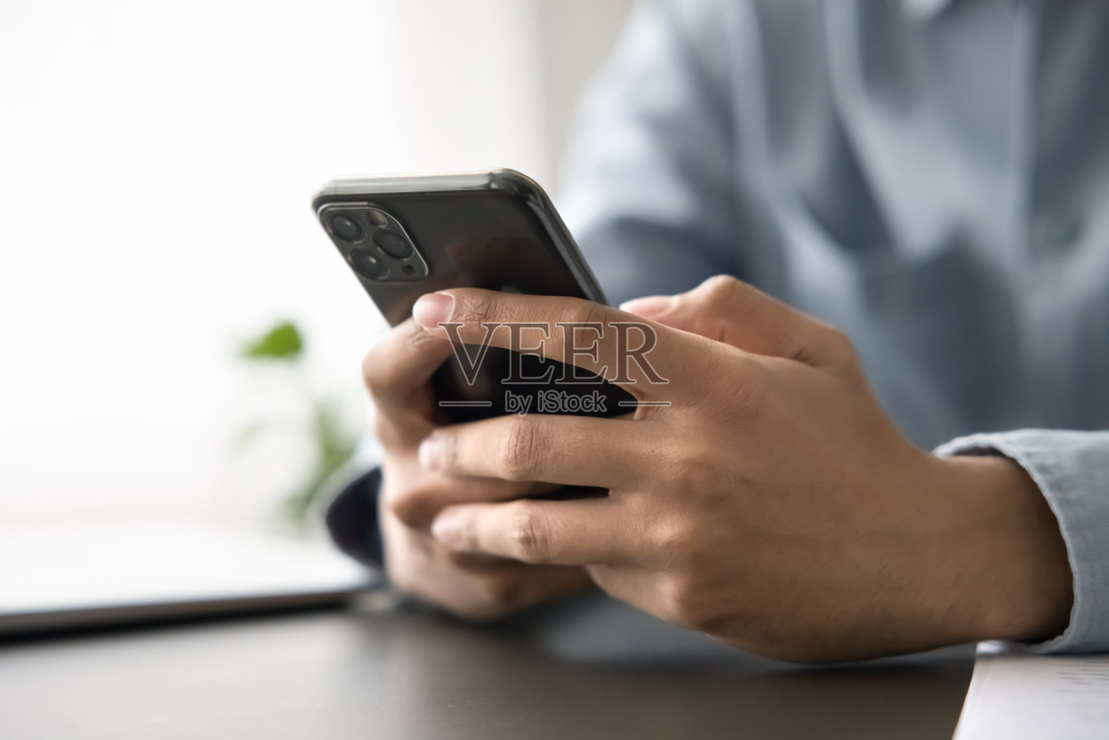 一个无法辨认的男人坐在桌子前，手中拿着智能手机照片摄影图片